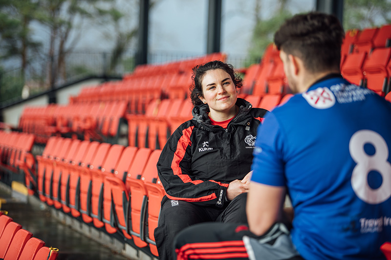 Staff Member and Student Sitting in seats of QUB Upper Malone Playing Fields Stadium 