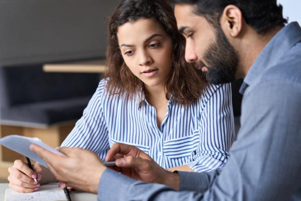 A woman writing into a notebook and a man reading through some papers next to her