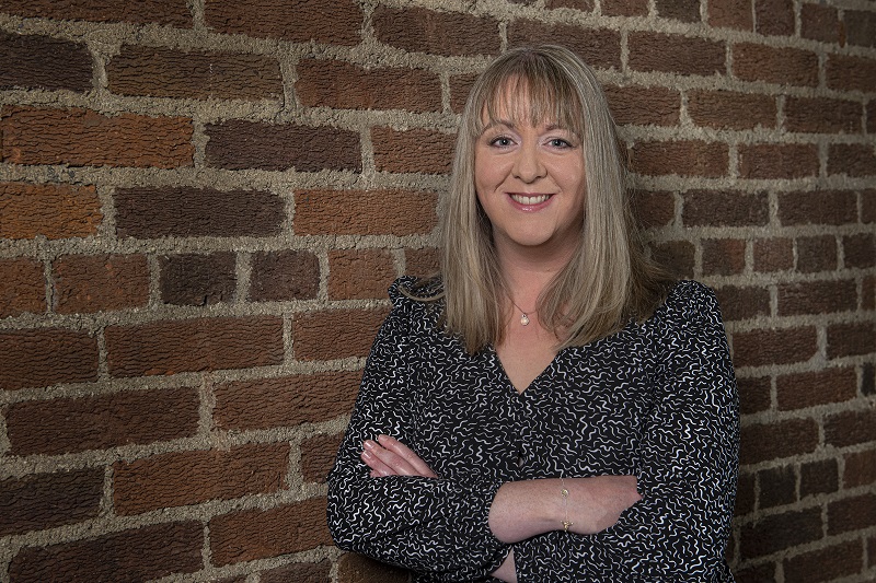 Dr Gemma Catney standing against a red brick wall