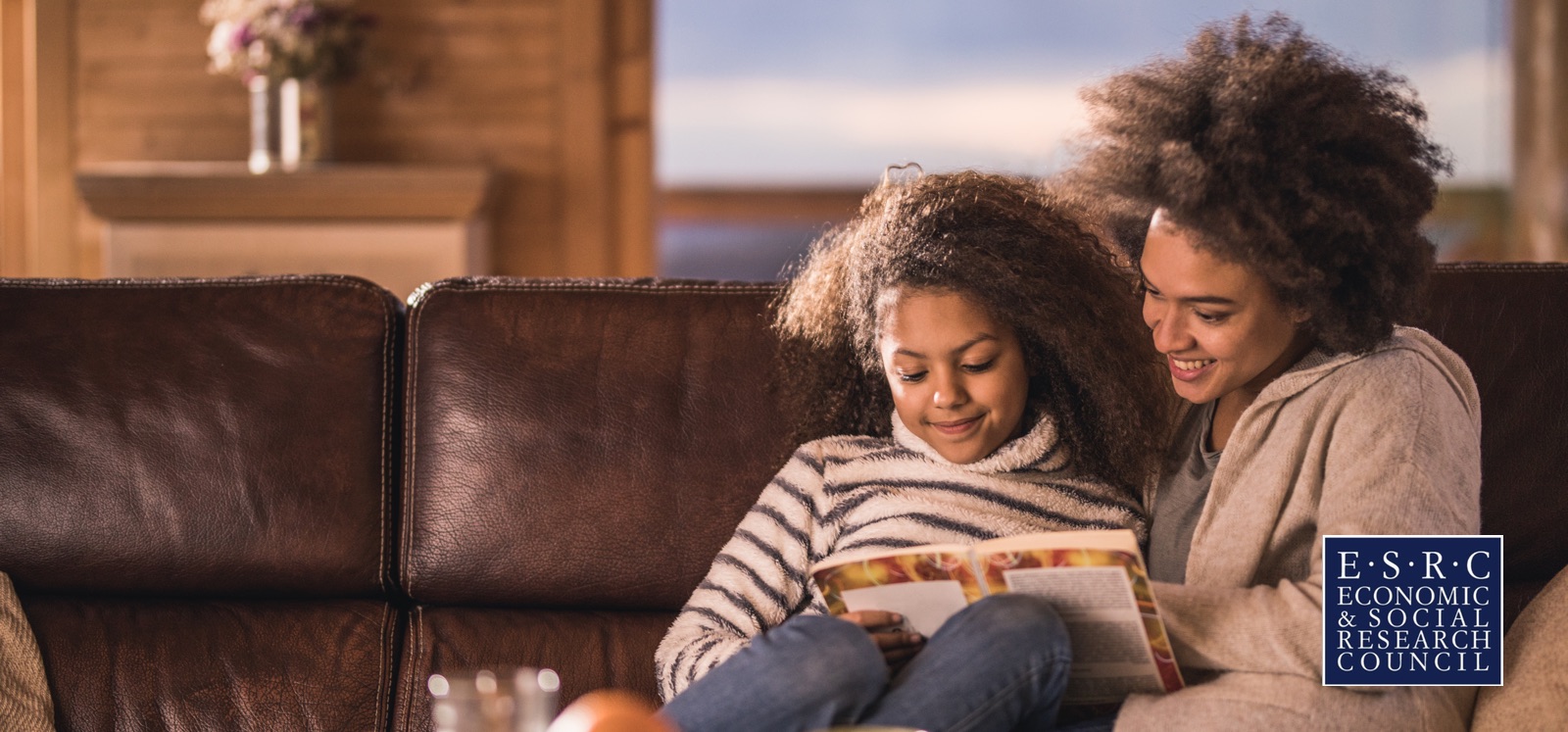 Mother and Daughter reading a book whilst sitting down.  Logo of Economic & Social Research Council