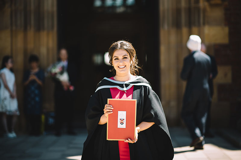 A happy student on Graduation day poses in front of the Lanyon