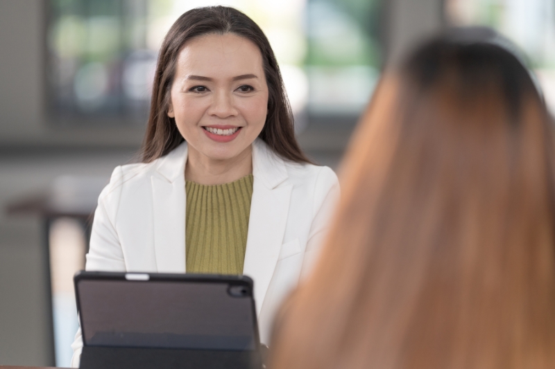 smiling woman with iPad chatting with another woman with their back to camera