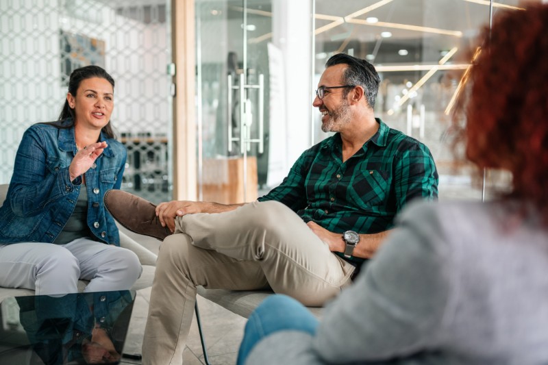 Smiling woman seated in a bright, glass-framed office talking to colleagues