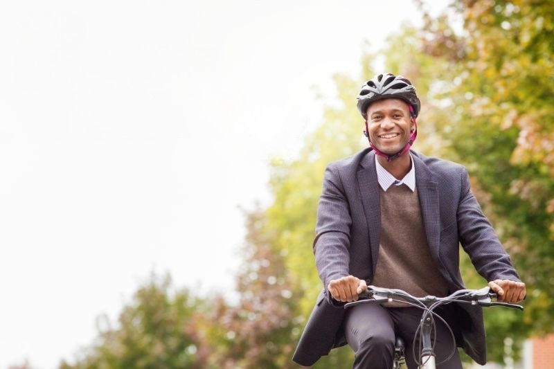smiling black man wearing bicycle helmet and cycling with trees in the right hand side background