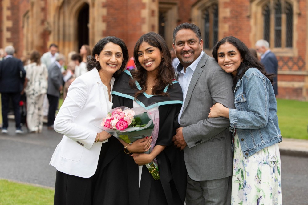 graduating young woman holding bouquet of flowers surrounded by family members and posing for a photo outside a redbrick building