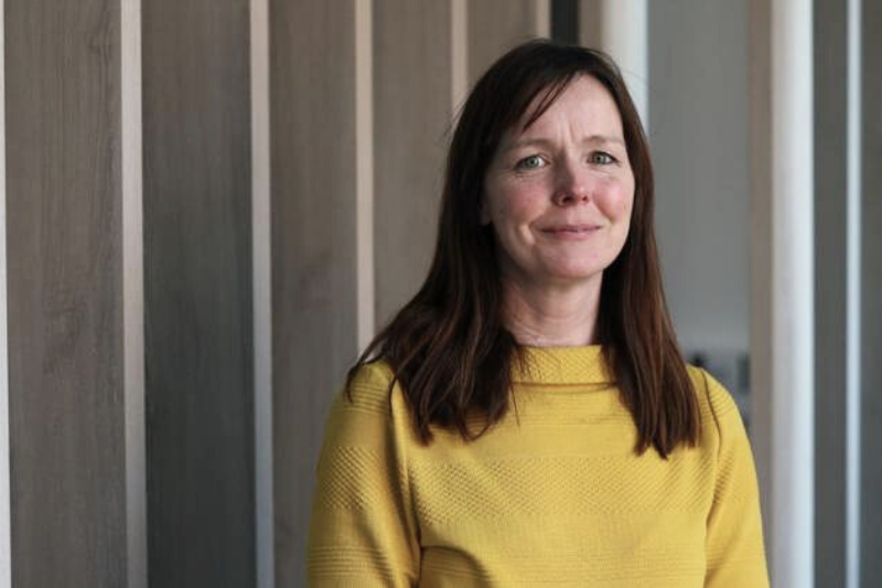 dark-haired woman in mustard-coloured knitted jumper smiling to camera