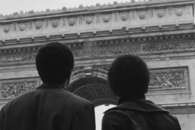 two black people pictured from the back looking up at what seems to be the famous arch on the Champs Elysées in Paris