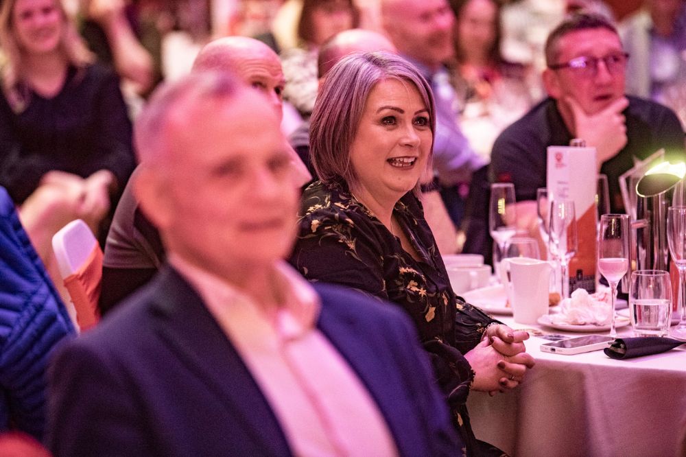 smiling woman seated at a table with others, watching something fun taking place off-camera
