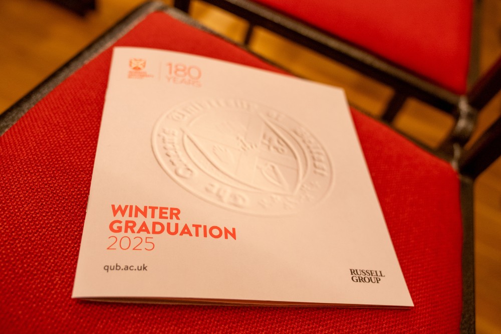 a Queen's University Belfast Winter Graduation 2025 programme brochure laid on a red chair